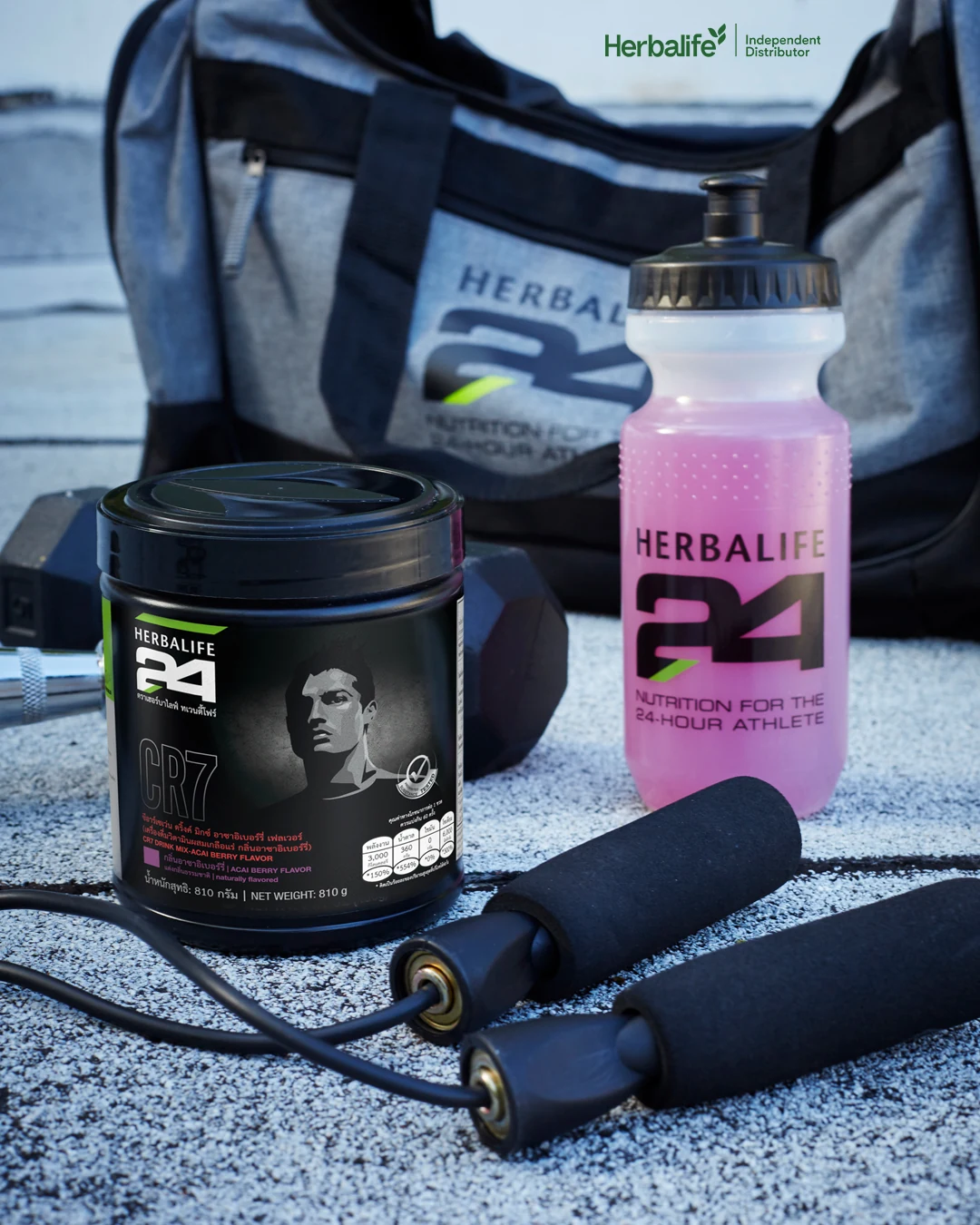 Black tub of drink powder, a pink water bottle, a skipping rope and a dumbbell in front of a sports bag