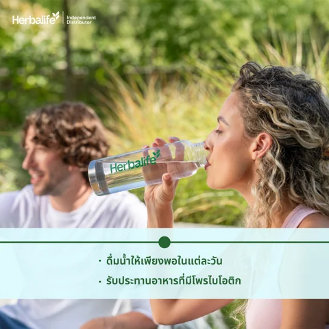 A woman in workout clothes sitting against a sofa, drinking from a shaker bottle (3/5)