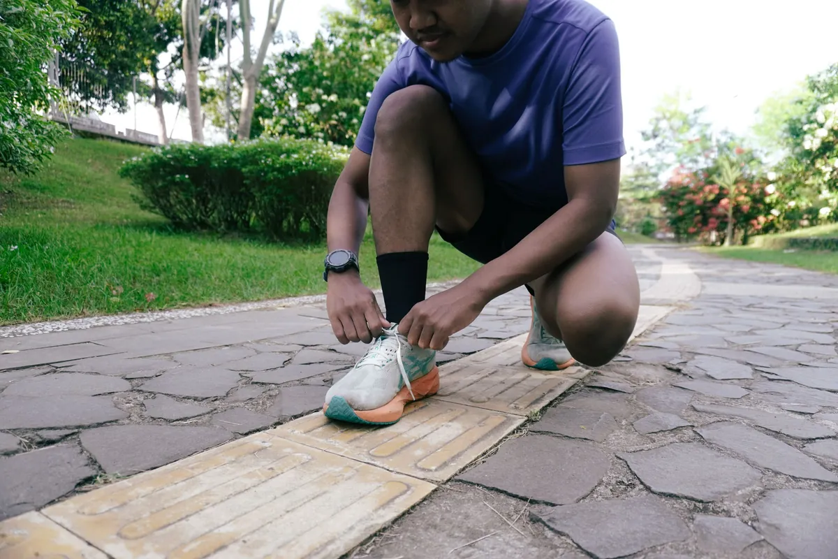 A man kneeling to tie his running shoes on a path in a park