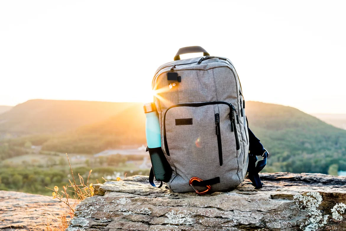 A hiking backpack with a water bottle on a rock surrounded by nature