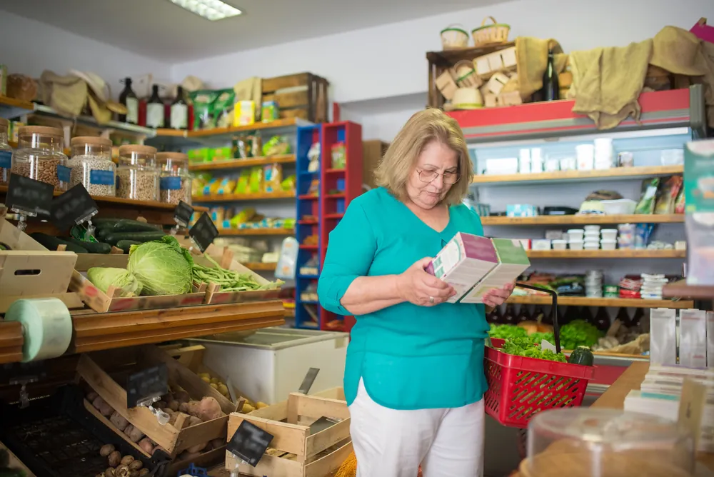 A woman in glasses comparing two food boxes in a grocery shop