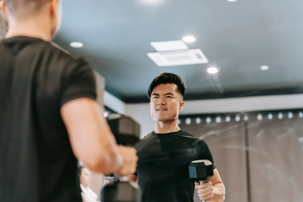 A man lifting dumbbells in front of a mirror at the gym
