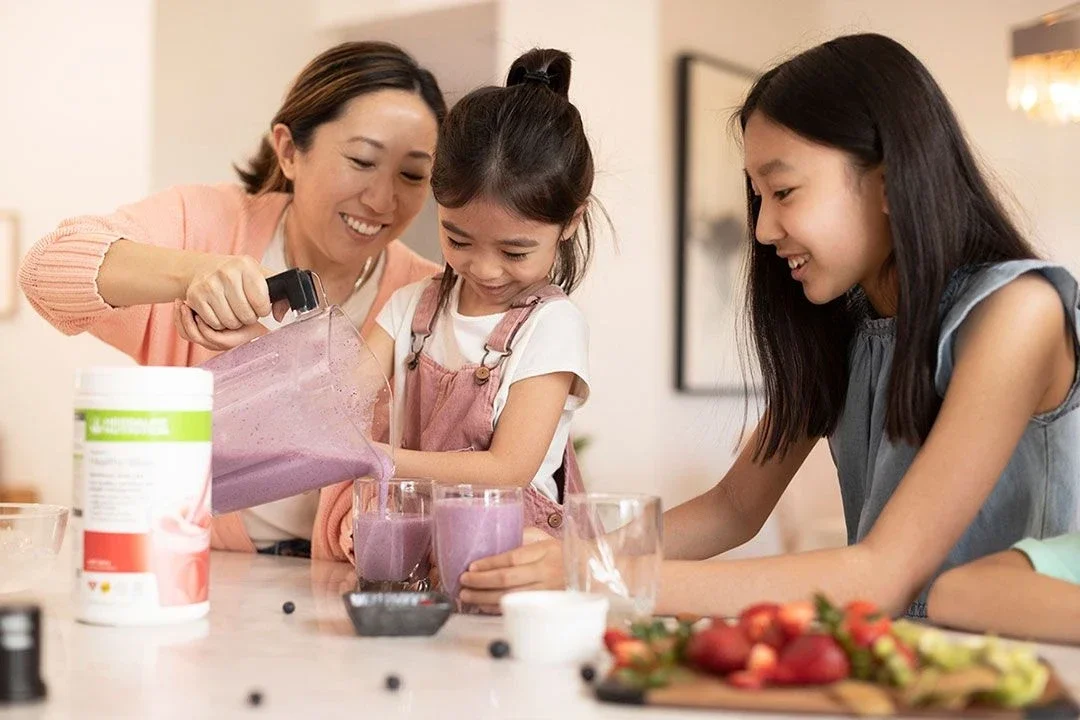 A mother and two daughters pouring a purple blended drink into glasses in the kitchen