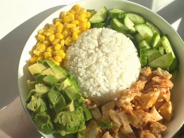 ชามข้าวกับอกไก่ อะโวคาโด ข้าวโพด และแตงกวา แยกเป็นส่วน ๆ